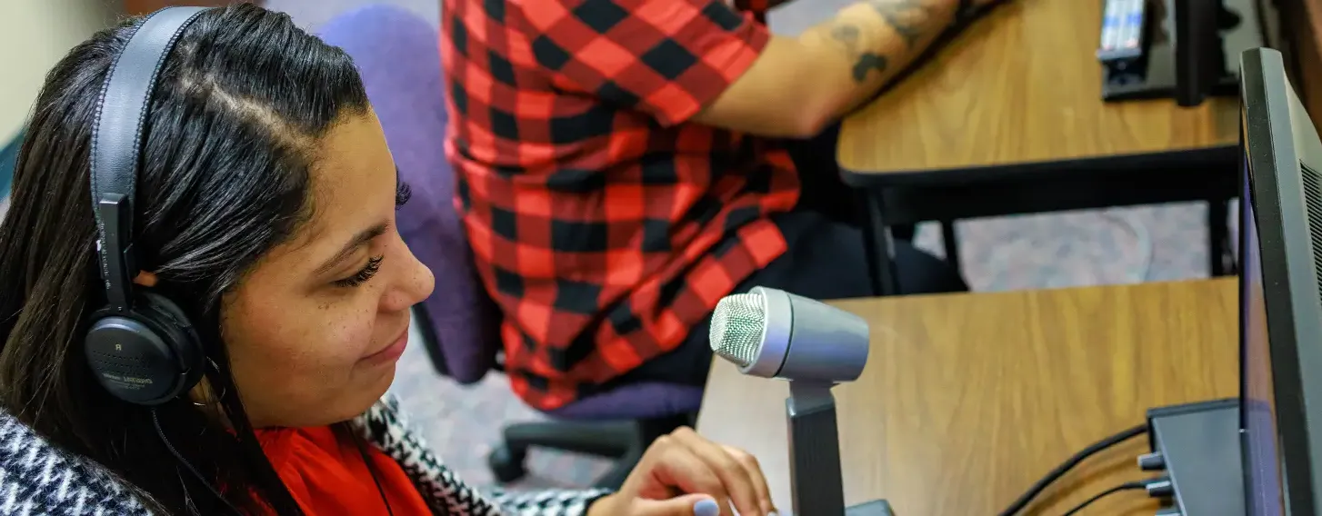 Two students wearing headphones and using microphones at desks with computers.